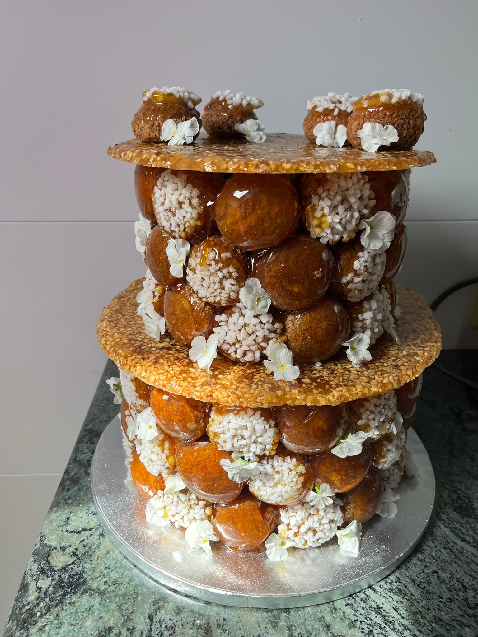 Pièce montée choux caramel et fleurs Pièce montée à étages de choux caramélisés, nougatine et fleurs blanches, cérémonie Montauban